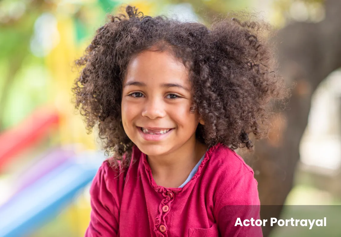 Young girl smiling with baby teeth missing, wearing a pink shirt. Actor portrayal.