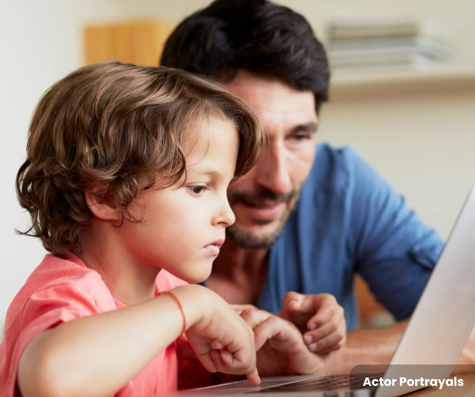 A young boy in a pink t-shirt and an adult, wearing a blue shirt, looking at a computer screen.