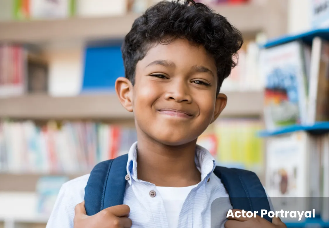 A smiling boy with a backpack, standing in front of a bookshelf. Actor Portrayal.