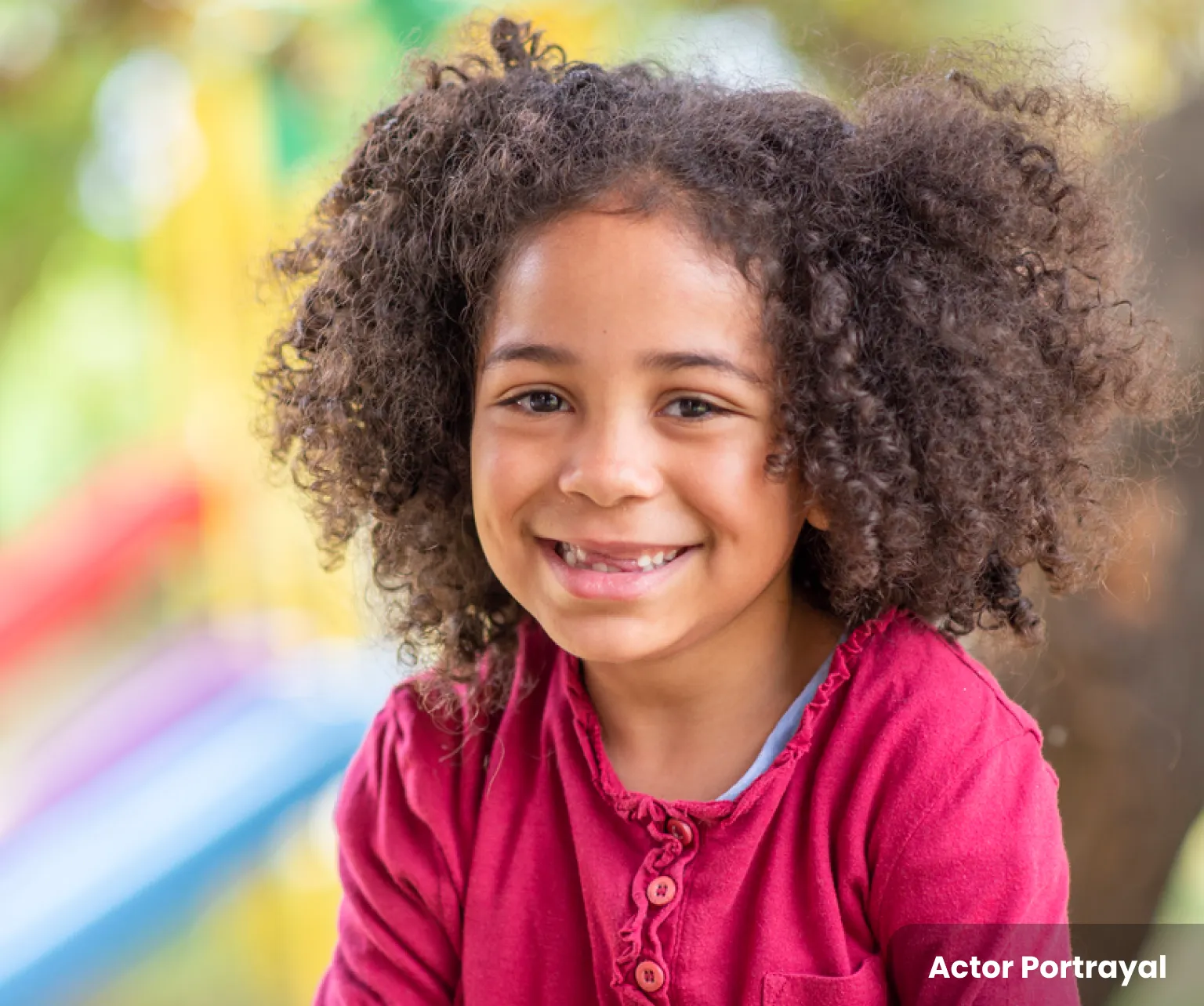 Young girl smiling with baby teeth missing, wearing a pink shirt. Actor portrayal.