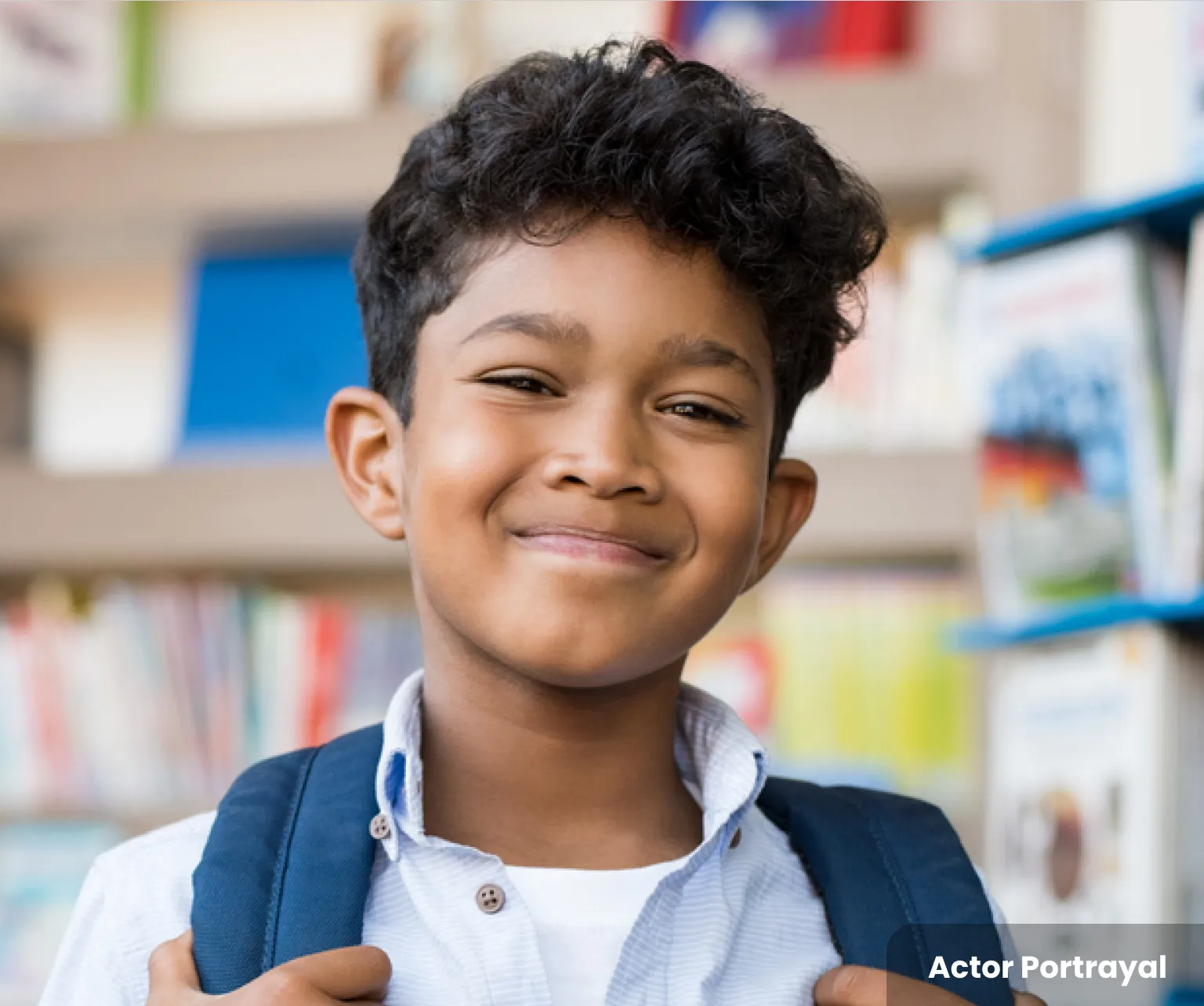 A smiling boy with a backpack, standing in front of a bookshelf. Actor Portrayal.
